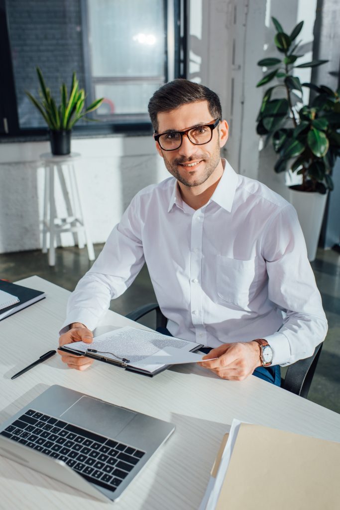 smiling male translator working with documents and laptop in office